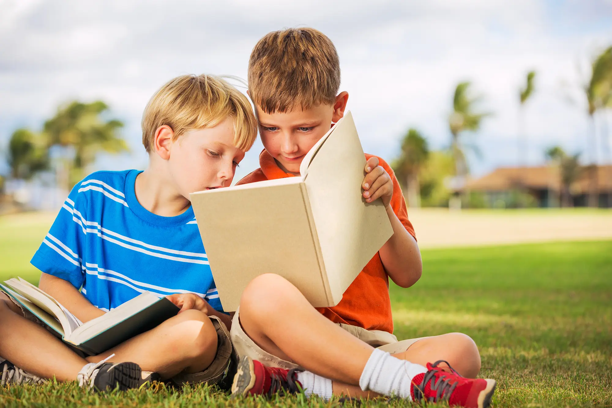 Two young boys reading books on the grass